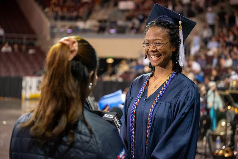 A Penn State Behrend graduate talks with a TV reporter before the college's commencement ceremony.